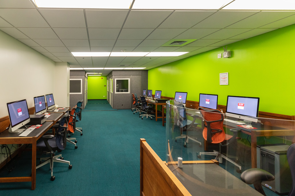 Digital Media Lab with bright green walls, a service desk, Mac desktop computers, scanners, and Music Booths in the background.