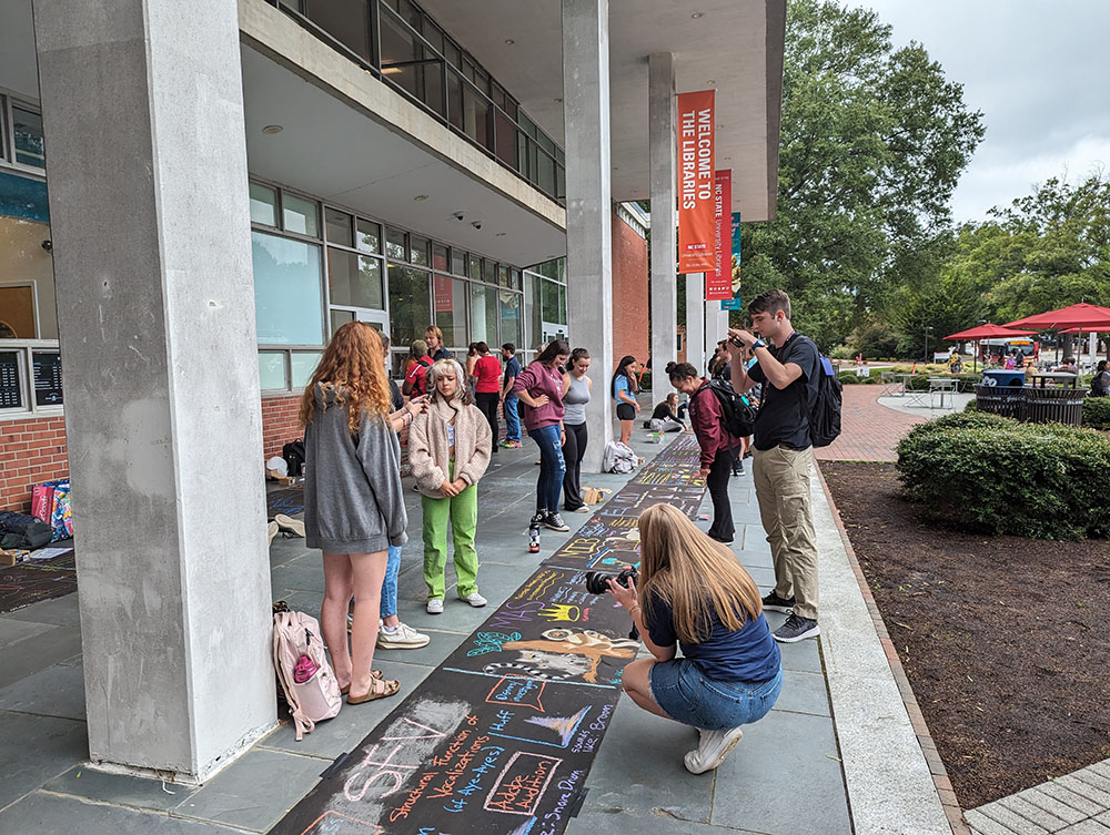 Students in front of the Hill Library, looking at the sidewalk.