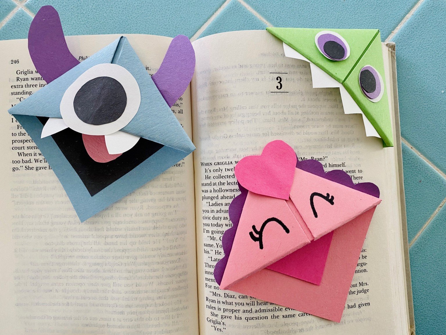 Blue, pink and green origami shaped bookmarks on a book.