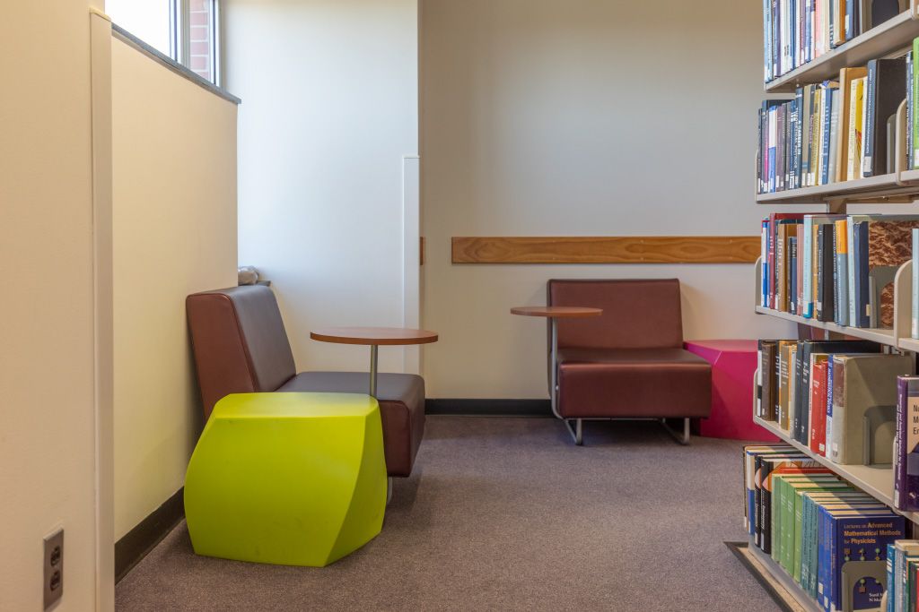 Soft seating with small attached writing surface on a swivel against walls facing bookshelves.