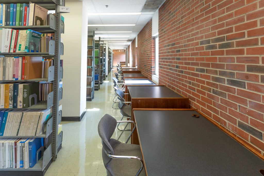 Small desks with moulded chairs facing a brick wall with exterior windows.