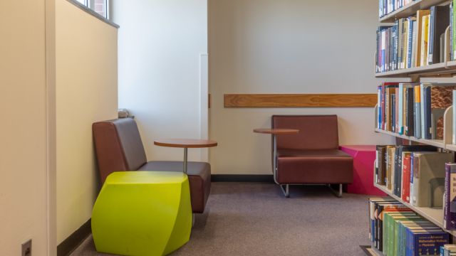 Soft seating with small attached writing surface on a swivel against walls facing bookshelves.