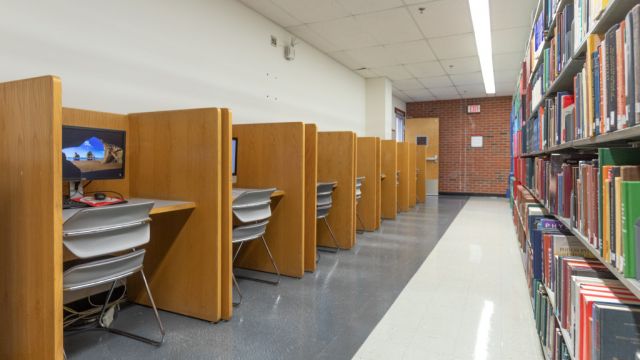 Individual carrels with moulded chairs and computers across from full bookshelves.